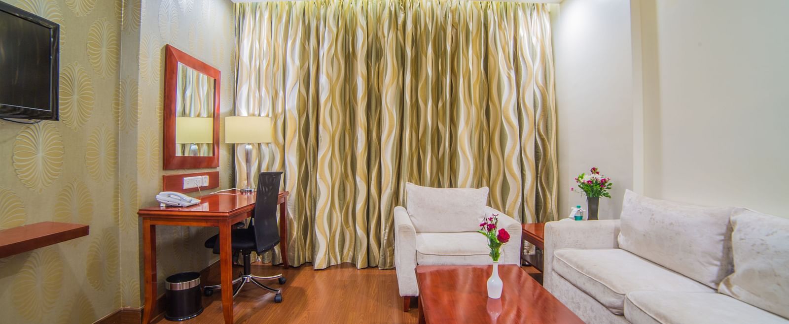 A hotel room with a clean, modern design, featuring a white sofa, work desk, and warm lighting A grand hotel suite with an opulent red and white decor, large bed, and seating area, reflecting a traditional style at Sitara Luxury Hotel in Hyderabad near Ram
