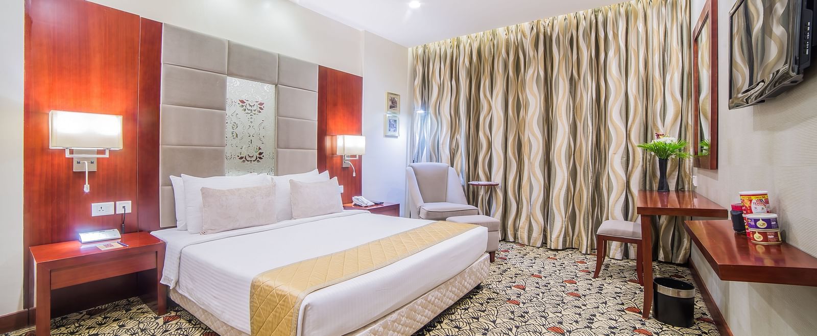 A spacious hotel room with crisp white bedding, a work desk, and tasteful deco A grand hotel suite with an opulent red and white decor, large bed, and seating area, reflecting a traditional style at Sitara Luxury Hotel in Hyderabad near Ramoji Film City.