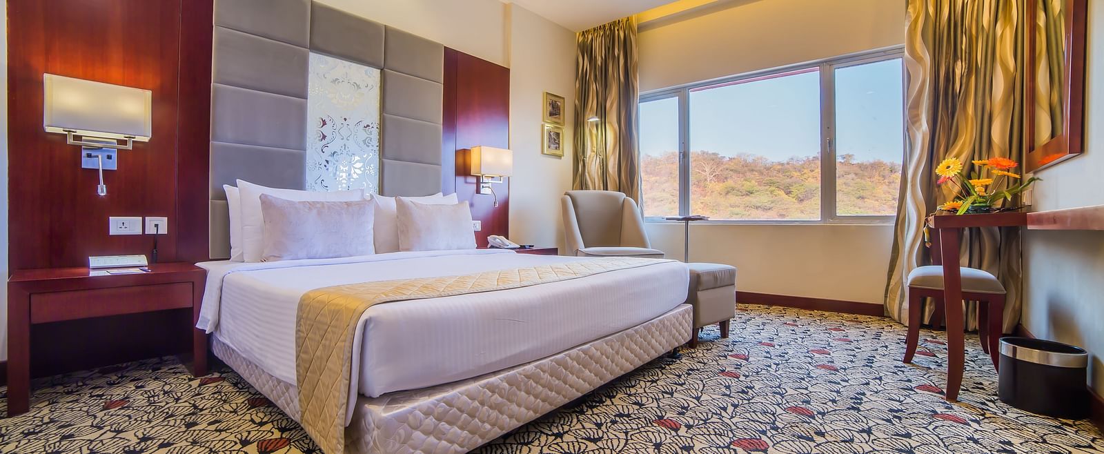 A luxurious hotel room with a plush white bed, warm accent lighting, and a scenic window view A grand hotel suite with an opulent red and white decor, large bed, and seating area, reflecting a traditional style at Sitara Luxury Hotel in Hyderabad near Ramo