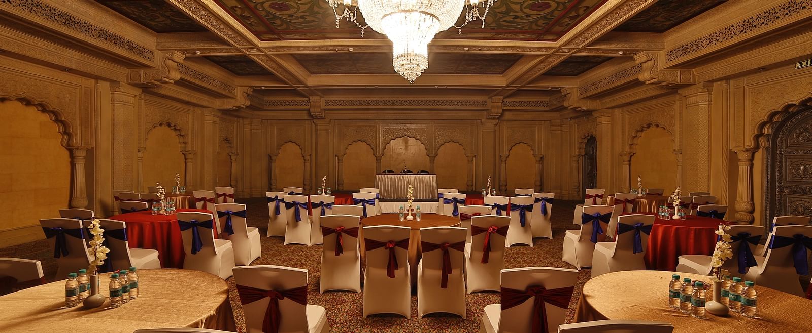 Seating arrangement in Taj Mahal Hall A grand hotel suite with an opulent red and white decor, large bed, and seating area, reflecting a traditional style at Sitara Luxury Hotel in Hyderabad near Ramoji Film City.