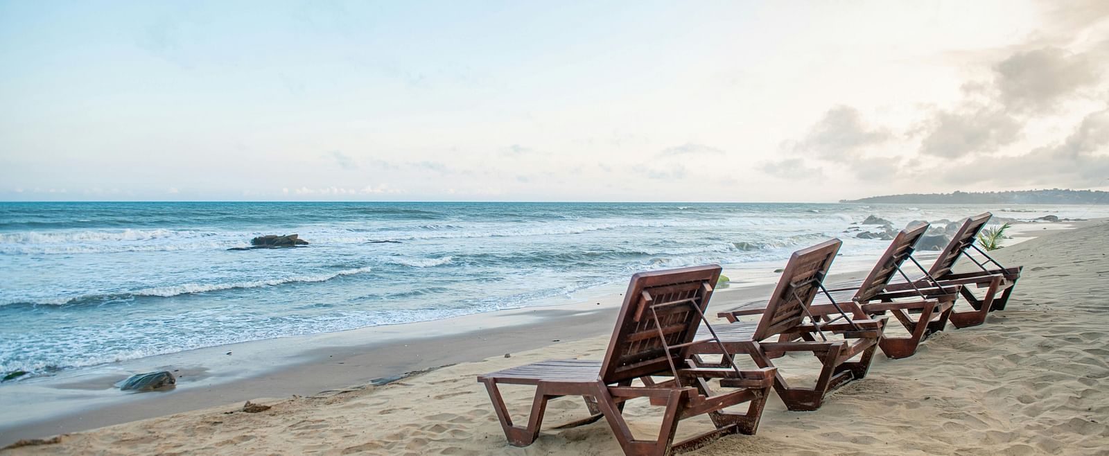 Wooden loungers placed in front of a shoreline on the beach during the day.