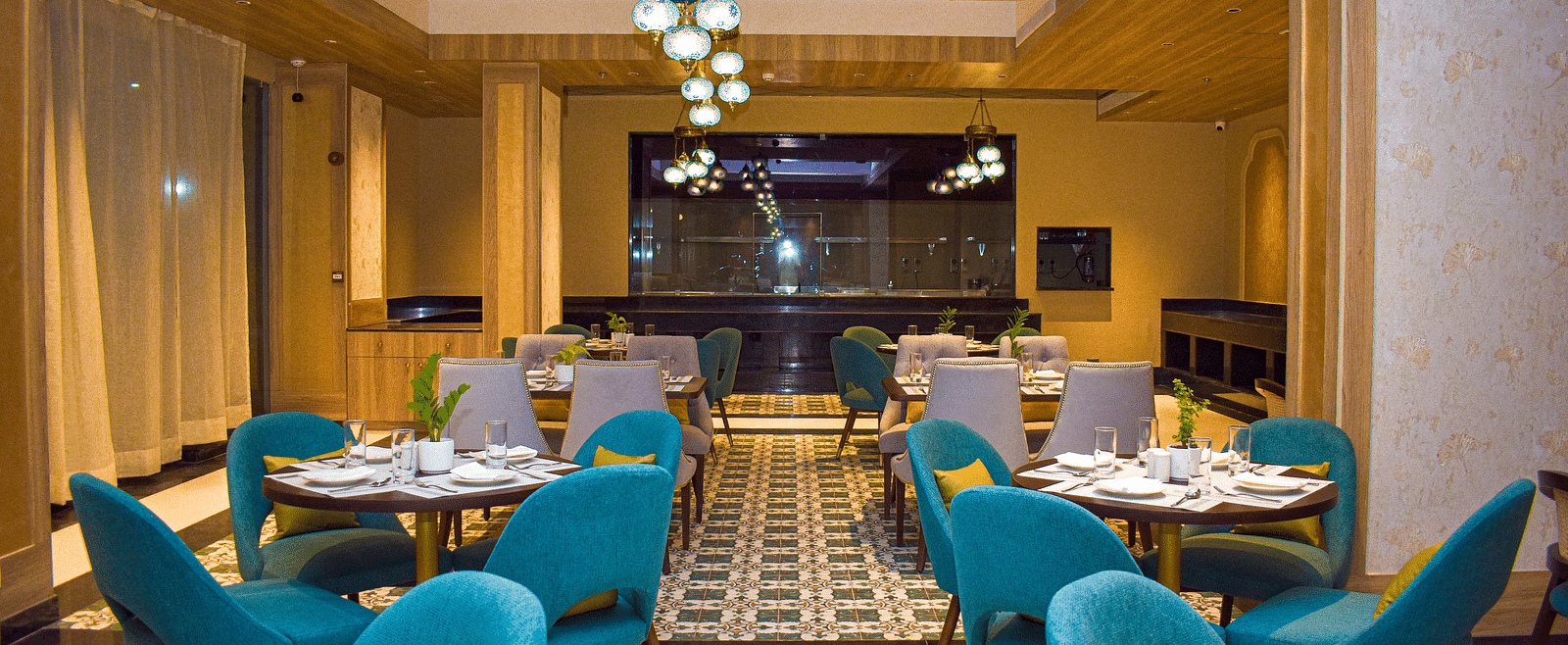 A modern restaurant interior with teal armchairs, round tables, patterned tile floor, and a distinctive globe chandelier - Urban Suites by BluSalzz, Jaipur