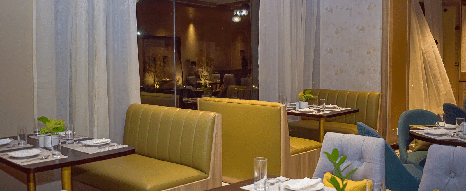 A restaurant interior with booth seating, set tables, sheer curtains, and hanging pendant lights - Urban Suites by BluSalzz, Jaipur