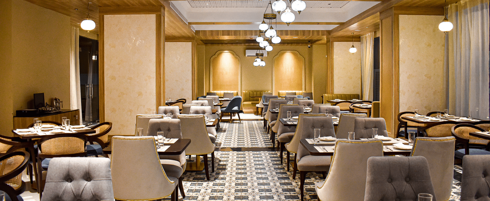 A restaurant interior with patterned tile floor, upholstered chairs, set tables, hanging pendant lights, and decorative ceiling panels - Urban Suites by BluSalzz, Jaipur