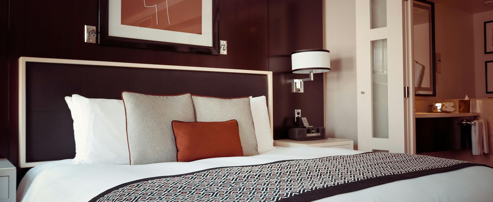 Interior of a stylish hotel room with a well-made bed and a glimpse into an adjacent bathroom.