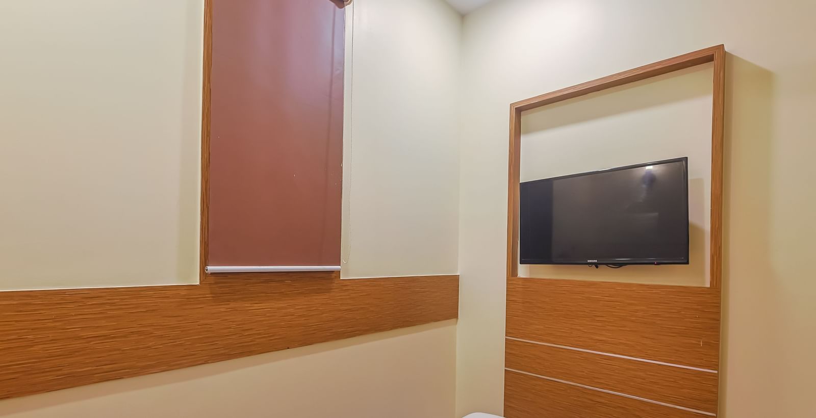 Bedroom with single bed, red runner, pillow, wooden wall panel and TV at Max Hotel Prayagraj.