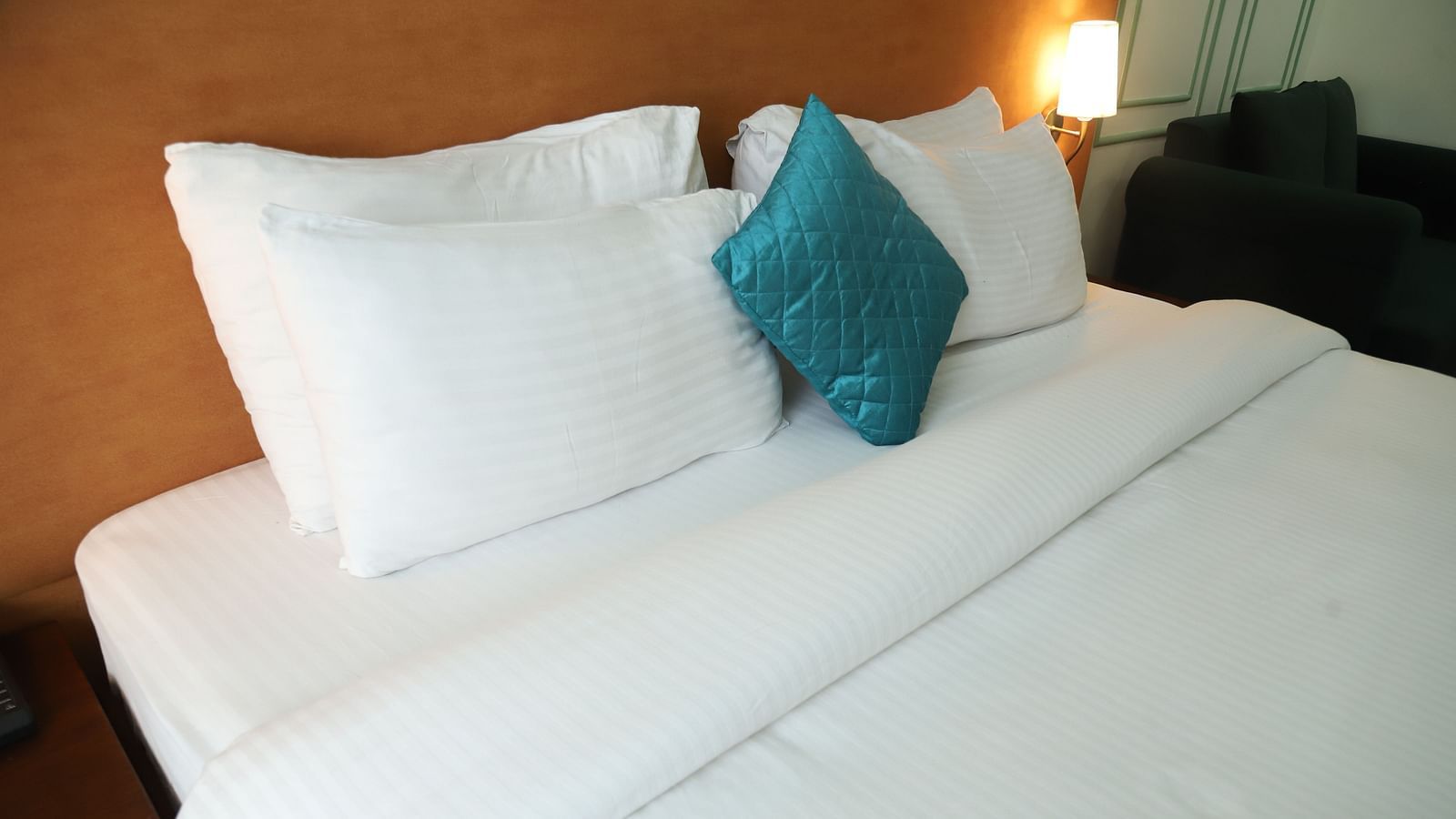 A close-up of a bed with white linens, several white pillows, and a single teal cushion - Asian Suites IFFCO Metro, Gurgaon