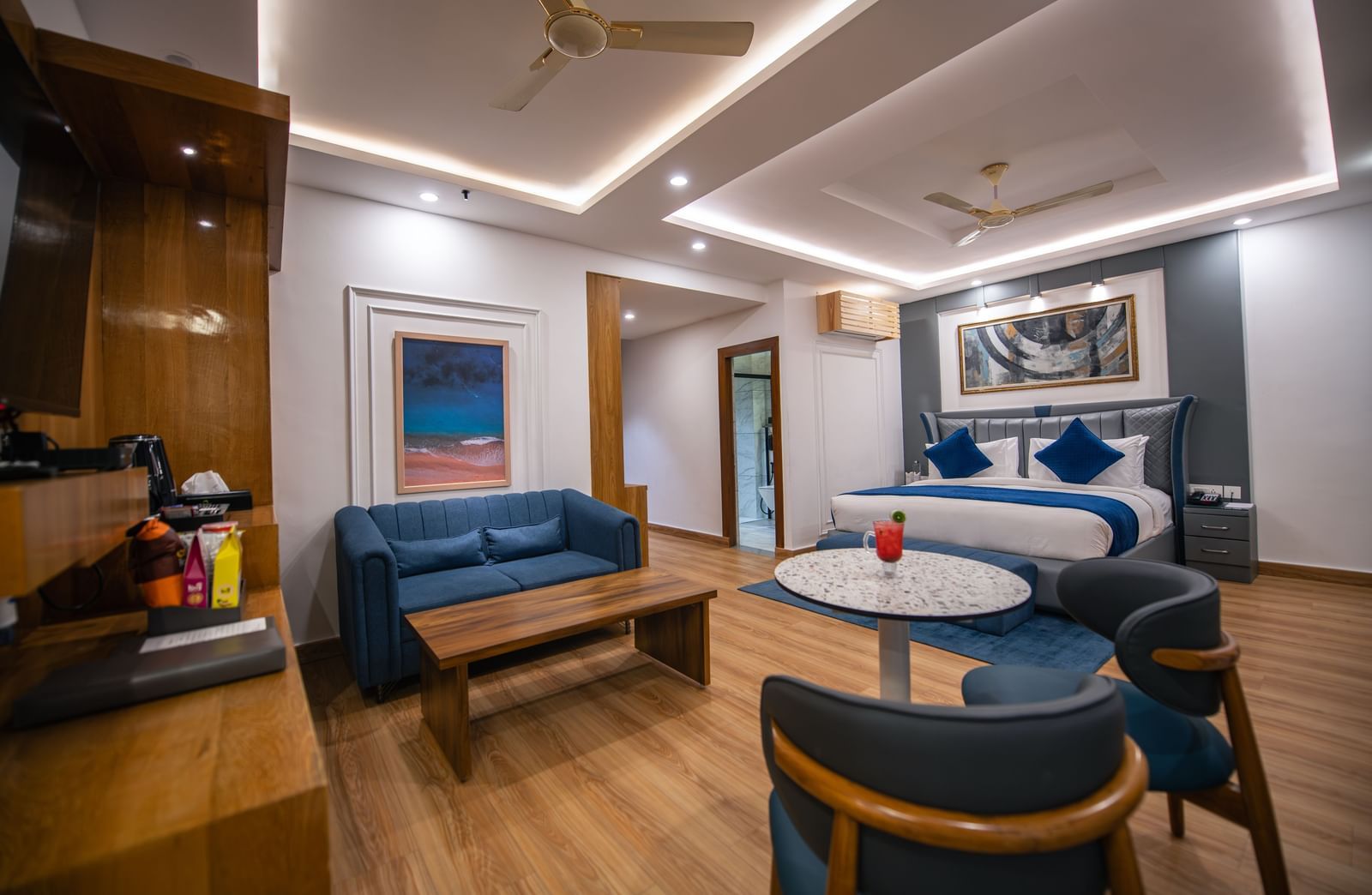 A spacious superior room at The Tattva Devaprayag with a bed featuring blue blankets, a sofa, and a round table.