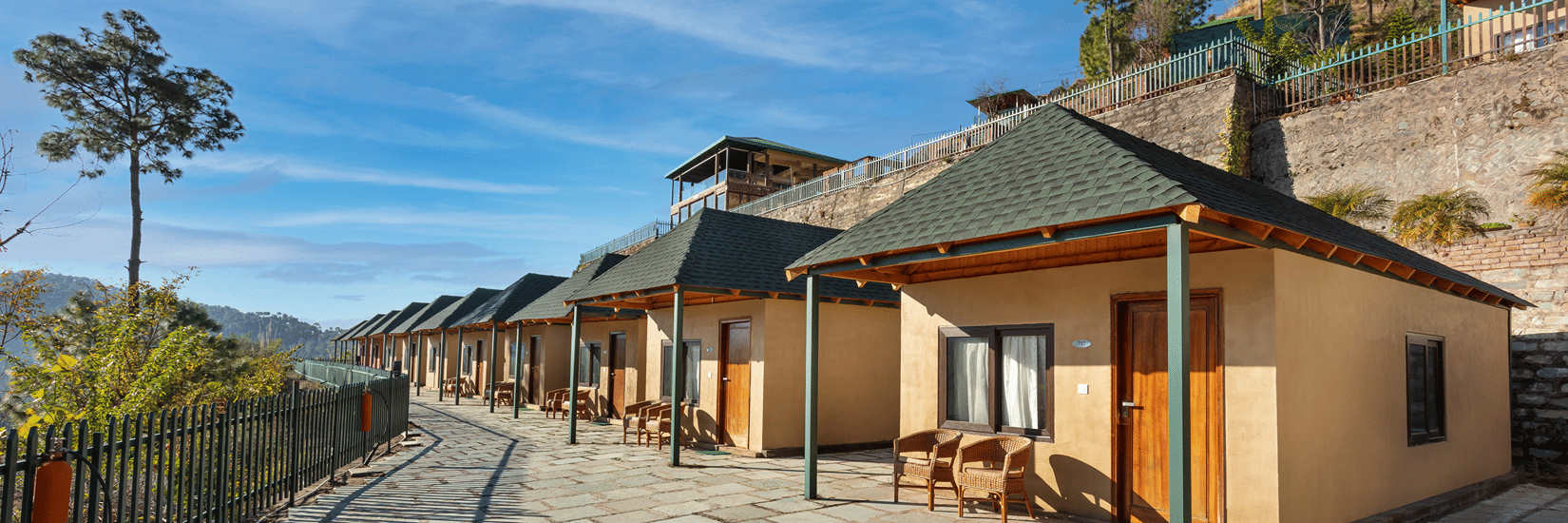 An image of cottage rooms from outside featuring a concrete yard at front and the entire villa is surrounded by trees in the hills - Suryavillas Luxury Resort and Spa, Solan