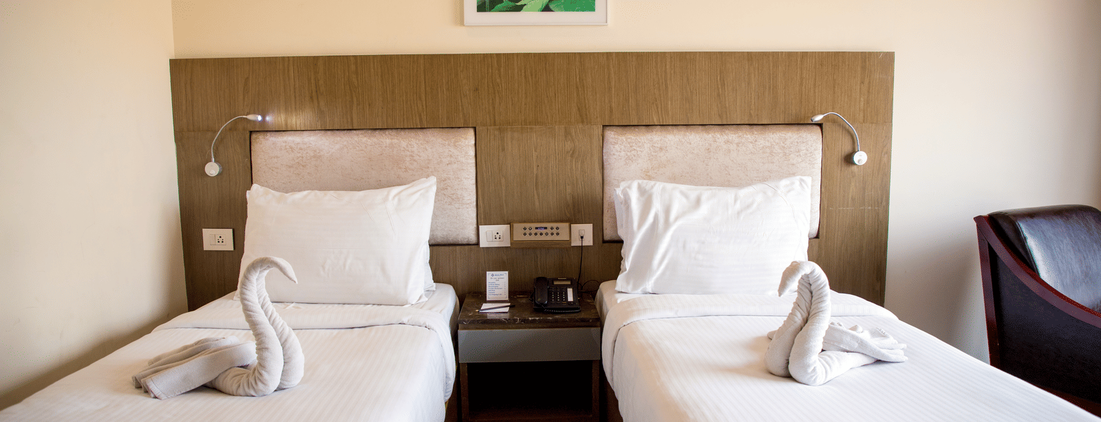 Close up shot featuring a twin beds in the Deluxe Room at Benzz Park, Vellore, with a bedside table between them.