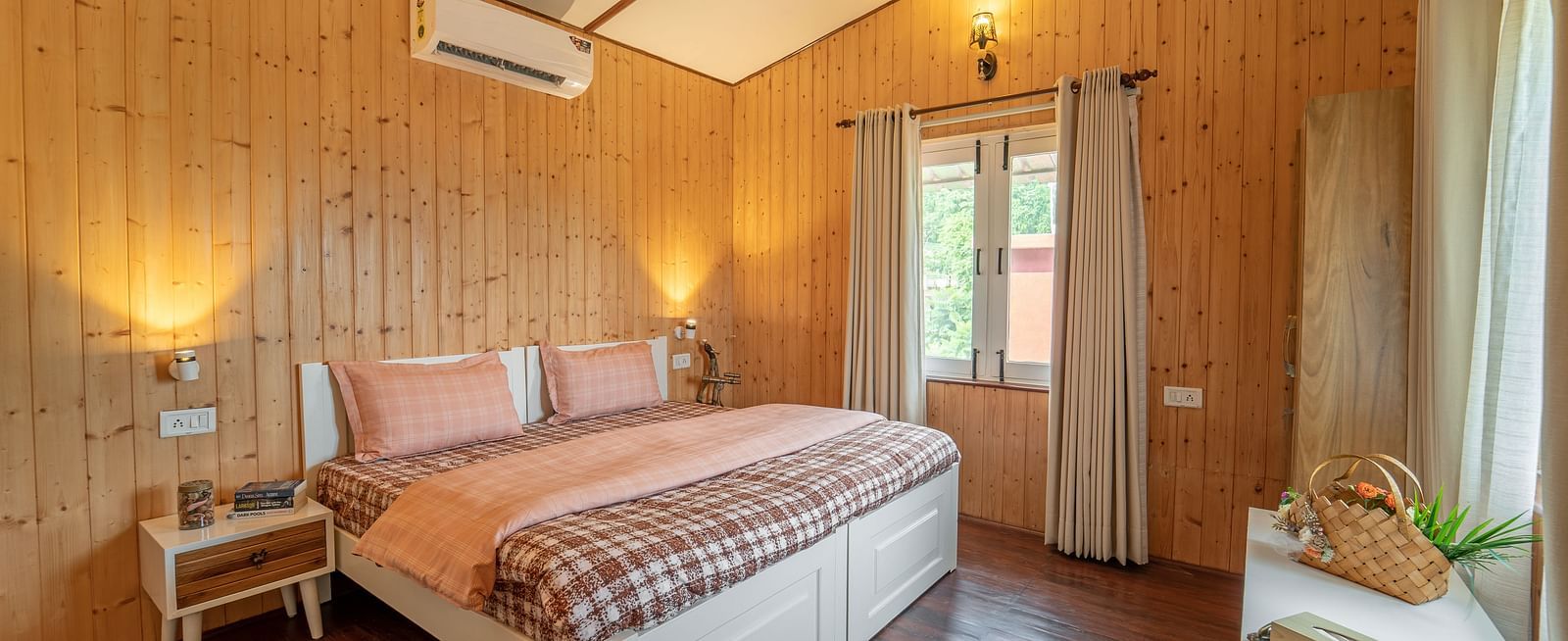 a double bed with side tables, lamps, and an ac wall mounted inside one of the rooms - neer ganga Resorts