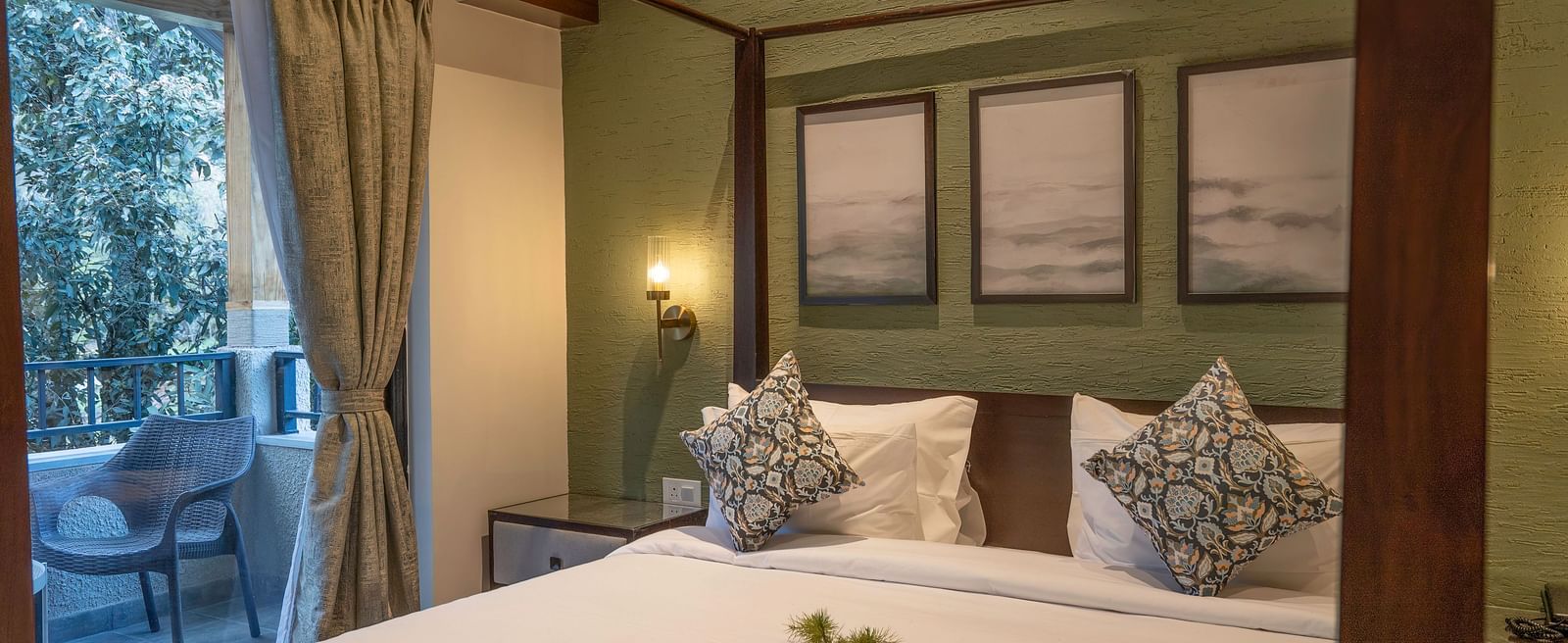 Four-poster bed with bedside tables and lamps, wall-mounted photographs above the headboard, and windows with curtains pulled to the side at The Chamomile Estate.