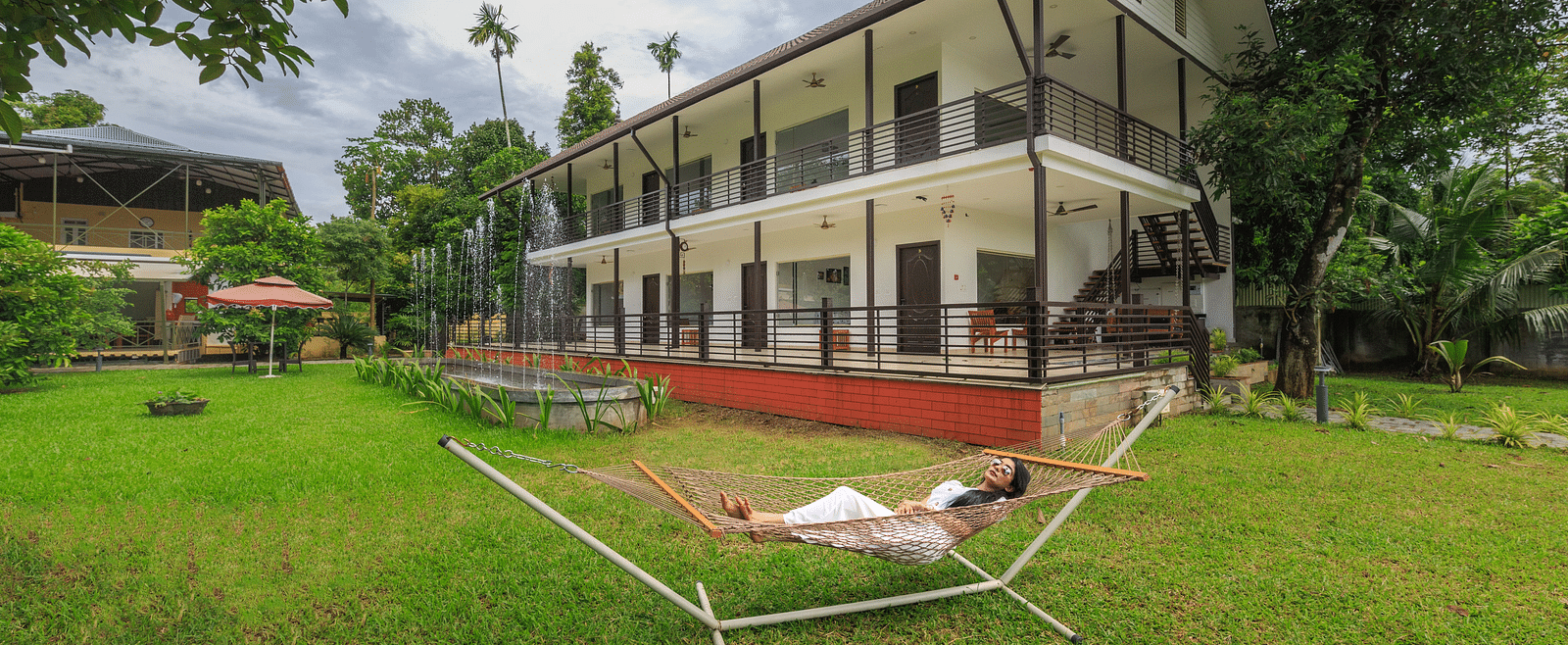 A person lying in a hammock in a grassy area in front of a large building with red accents.