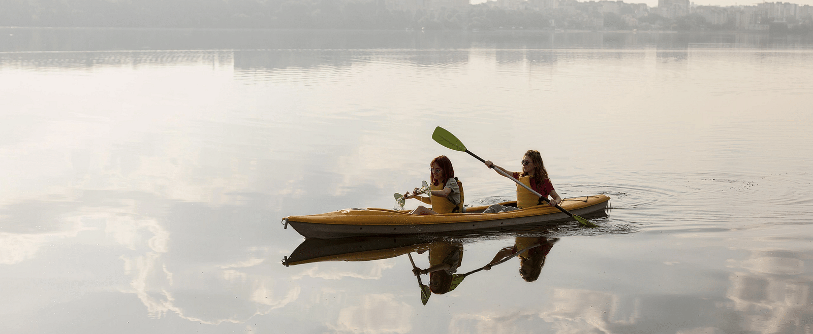 A small boat with two people paddling on a calm body of water under an overcast sky.