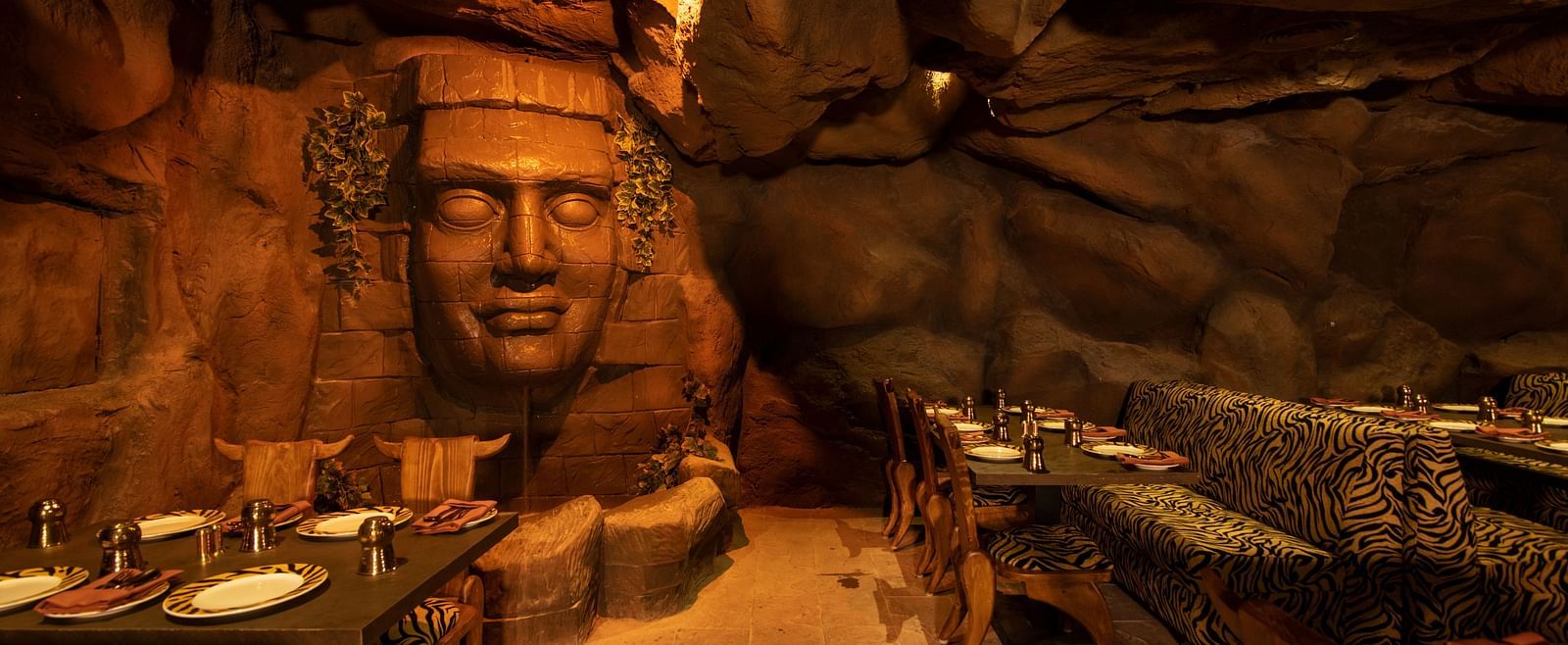 An image of interior view of a restaurant featuring a head sculpture and a rock wall -The President Hotel, Kumara Park, Bangalore