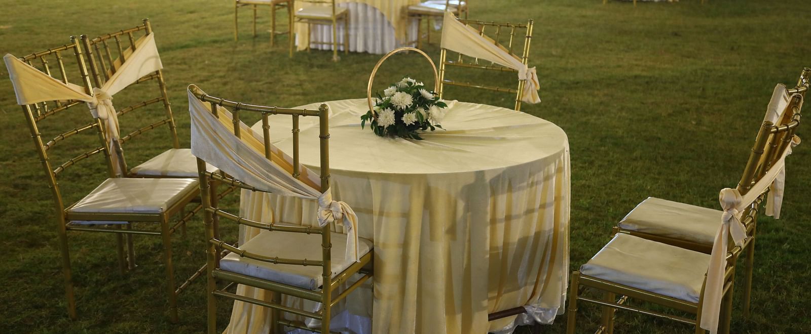 Round table setup with chairs in an open lawn event area at Tisya Farms, Gurgaon.