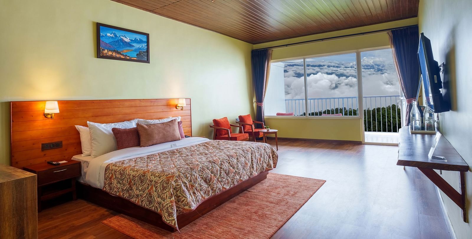 A tastefully decorated hotel room at Summit Enigma Resort & Spa, Lamahatta, with a large bed, a television, and a balcony offering an outdoor vista.