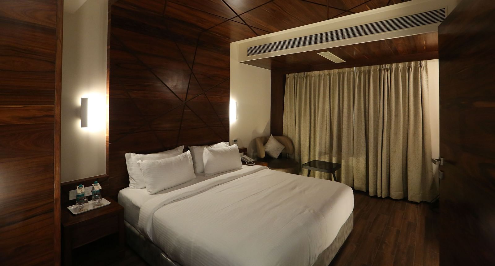 Premium Suite featuring a king size bed, bedside tables, lamps, and dark wood panelling - TGI SPS Grand, Coimbatore