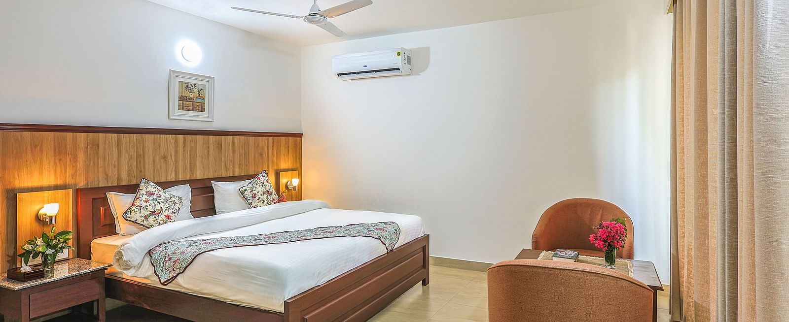 a double bed with side tables, lamps and chairs opposite it inside one of the rooms - Neer ganga Resorts