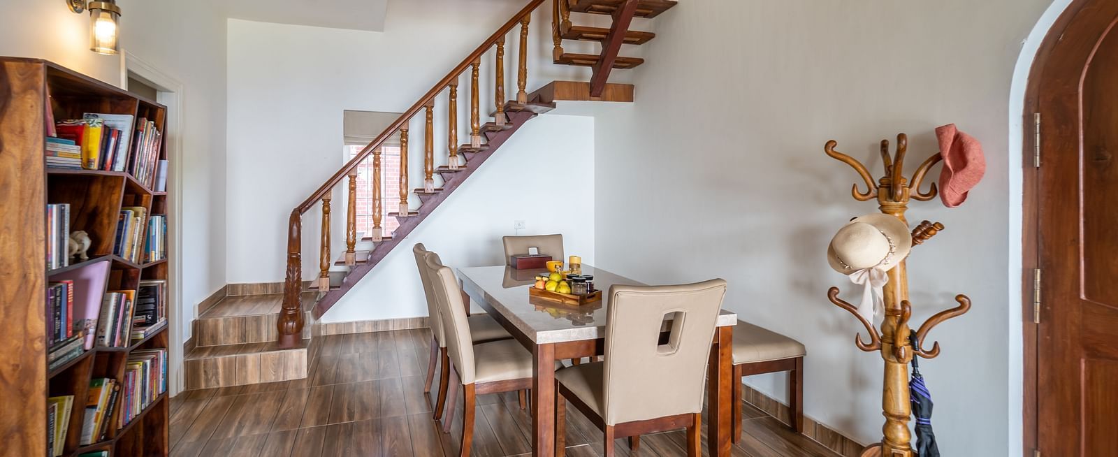 a dining area in view with a bookcase next to it and stairs in the background - neer ganga Resorts