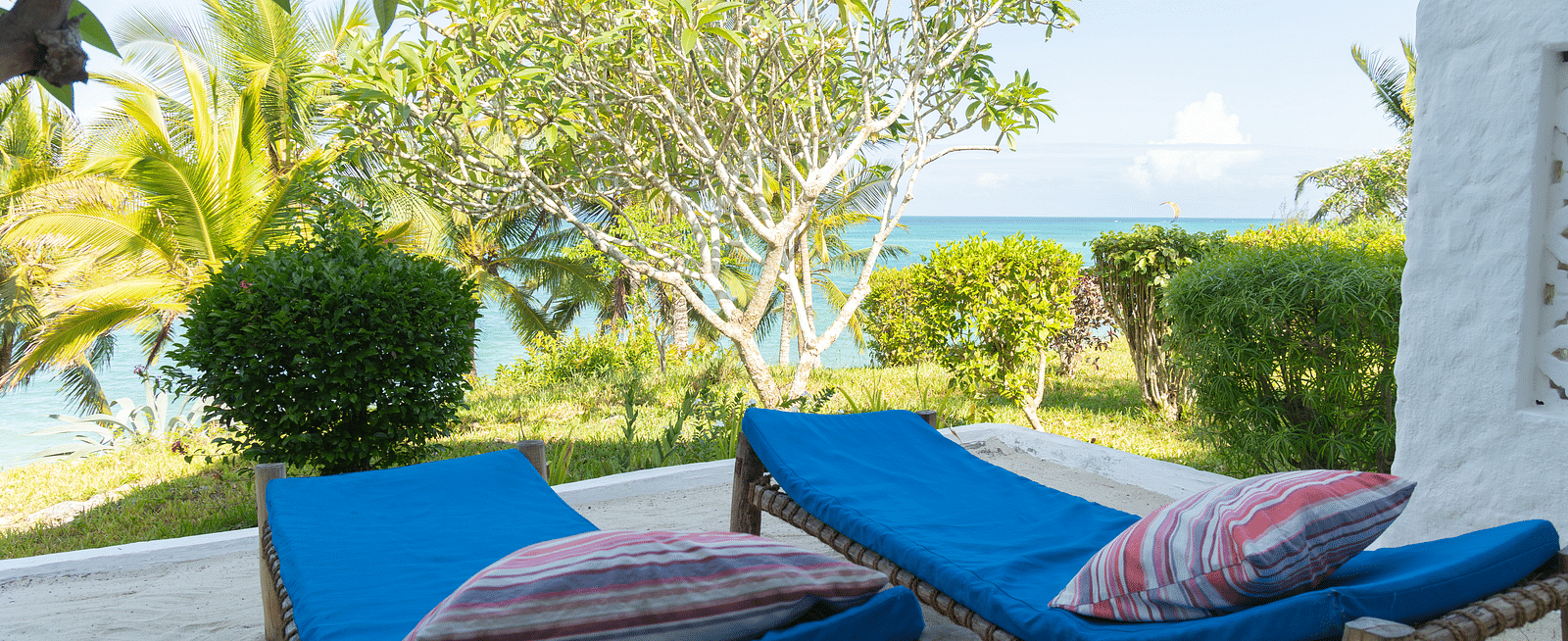 Outdoor seating area with blue sun loungers overlooking a tropical garden with vibrant foliage - Shooting Star Boutique Hotel.