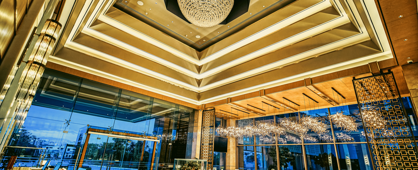 A grand hotel entrance with a central fountain, expansive windows, and elegant lighting - Grand Madurai by GRT Hotels