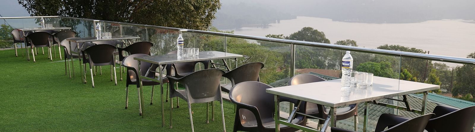 An image of the Lake View Oasis restaurant with chairs and tables at the rooftop and mountains and lake view in the background - Nisarga Lake Resort