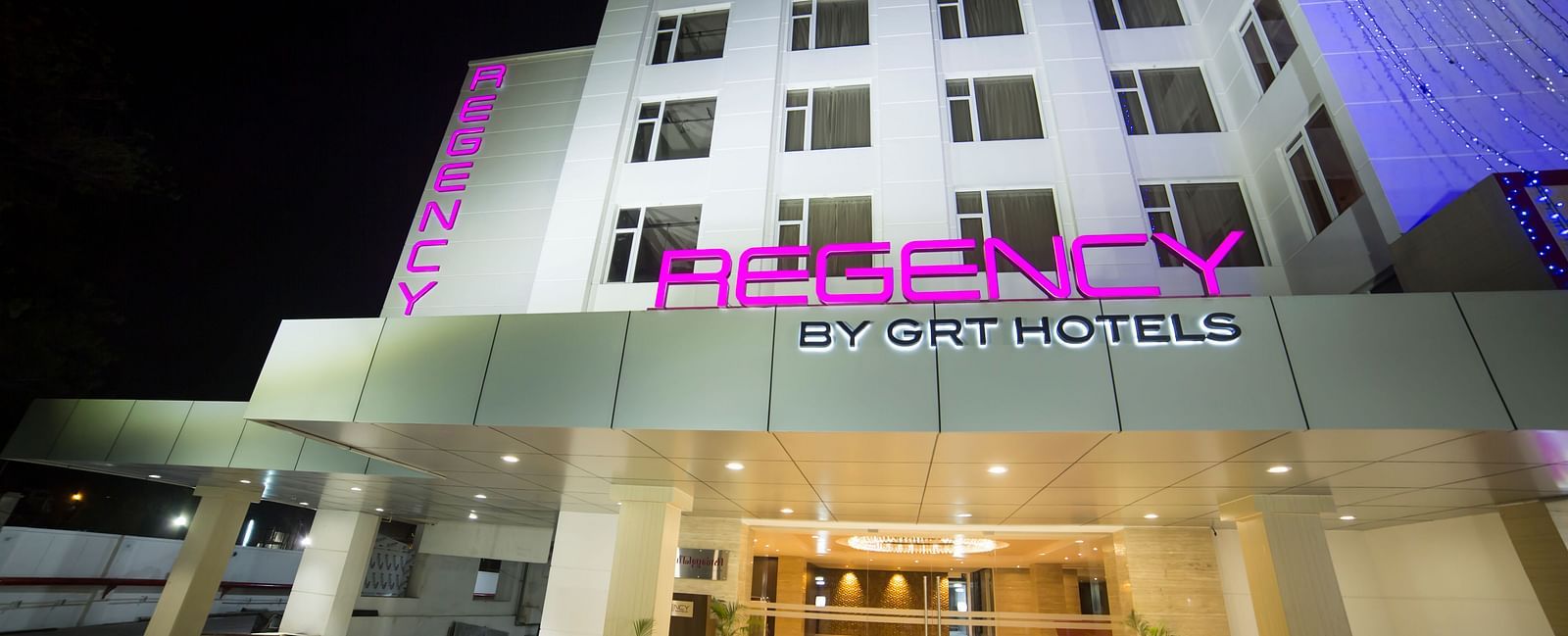 Regency GRT Hotels sign with purple letters and blue lights at night.