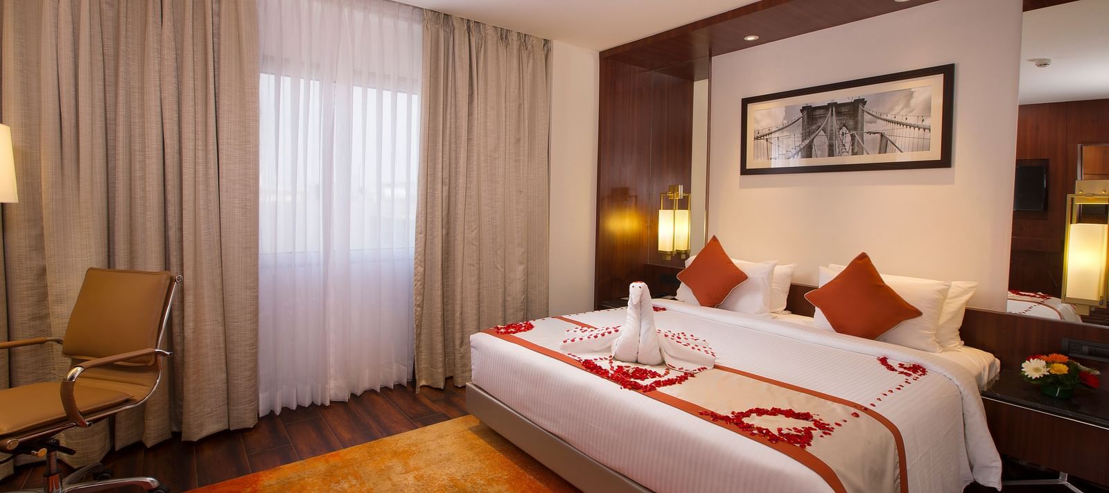 A hotel room with a large bed with white and orange linens, a brown office chair and sheer curtains over a window - Hotel Southend by TGI - Bommasandra, Bangalore