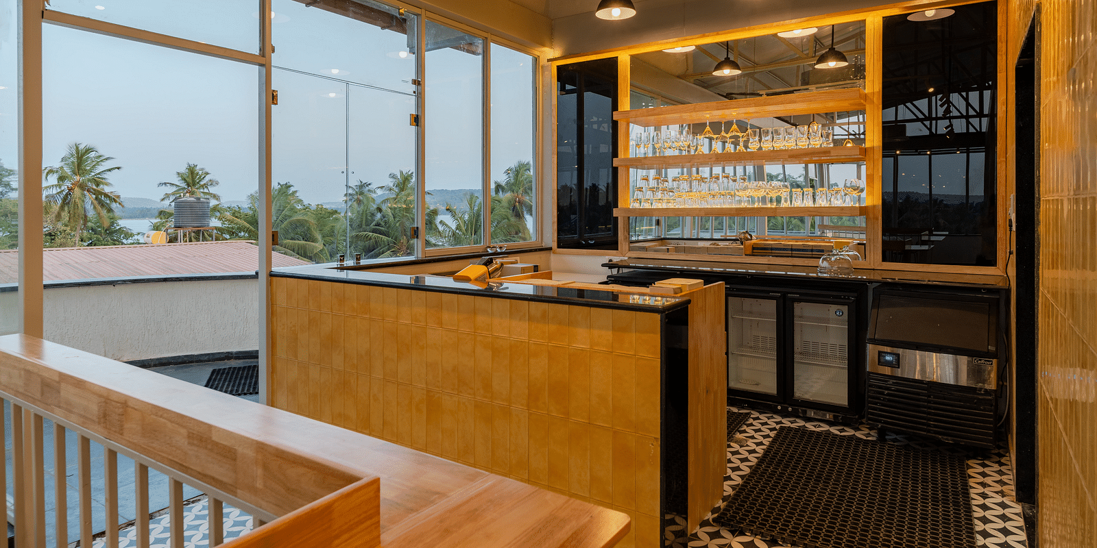 An elegant bar area with a wooden counter and backlit shelves, creating a sophisticated space for guests to enjoy a selection of fine wines and spirits in a modern, yet cosy ambiance  at Bedzzz Xclusiv Morjim, Goa