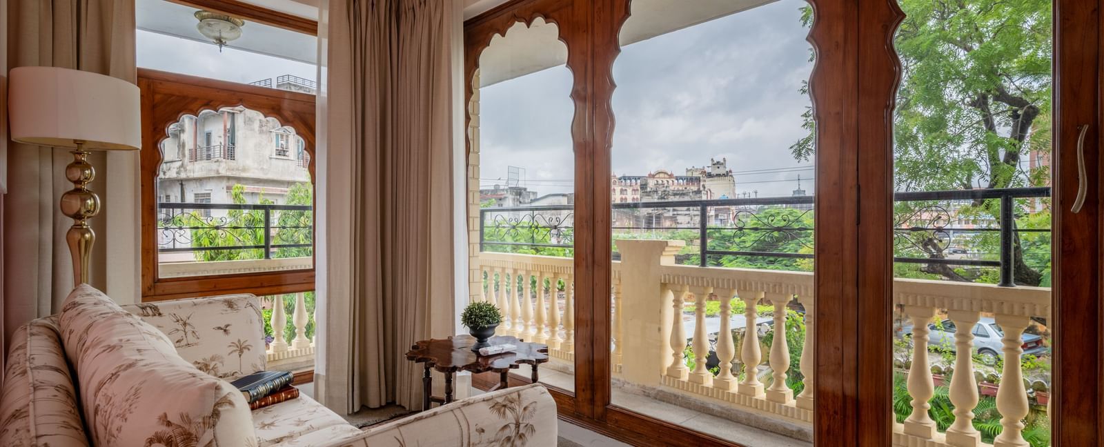 Sitting room with upholstered furniture, large arched windows, and views of greenery at Dera Rawatsar, Jaipur.