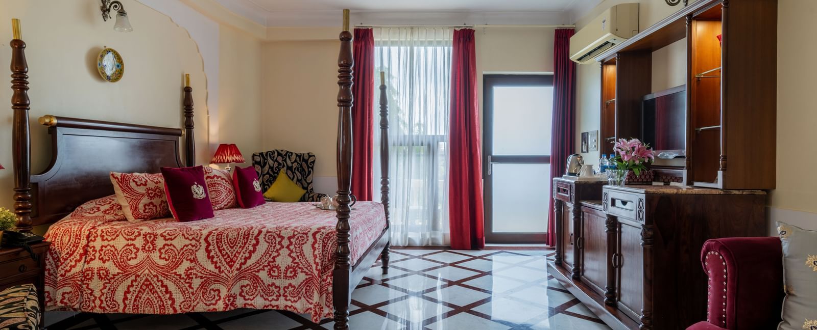  Bedroom with floral bedspread, wooden furniture, and doors opening to balcony at Dera Rawatsar, Jaipur.