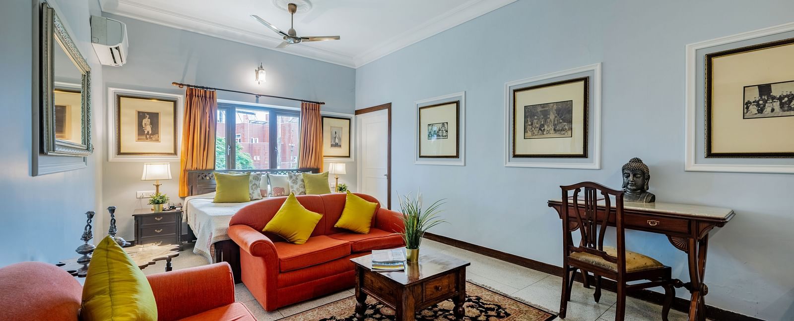 A well-lit suite at Dera Rawatsar in Jaipur offers comfortable seating, a wooden desk, framed artwork, and a glimpse into the sleeping area.
