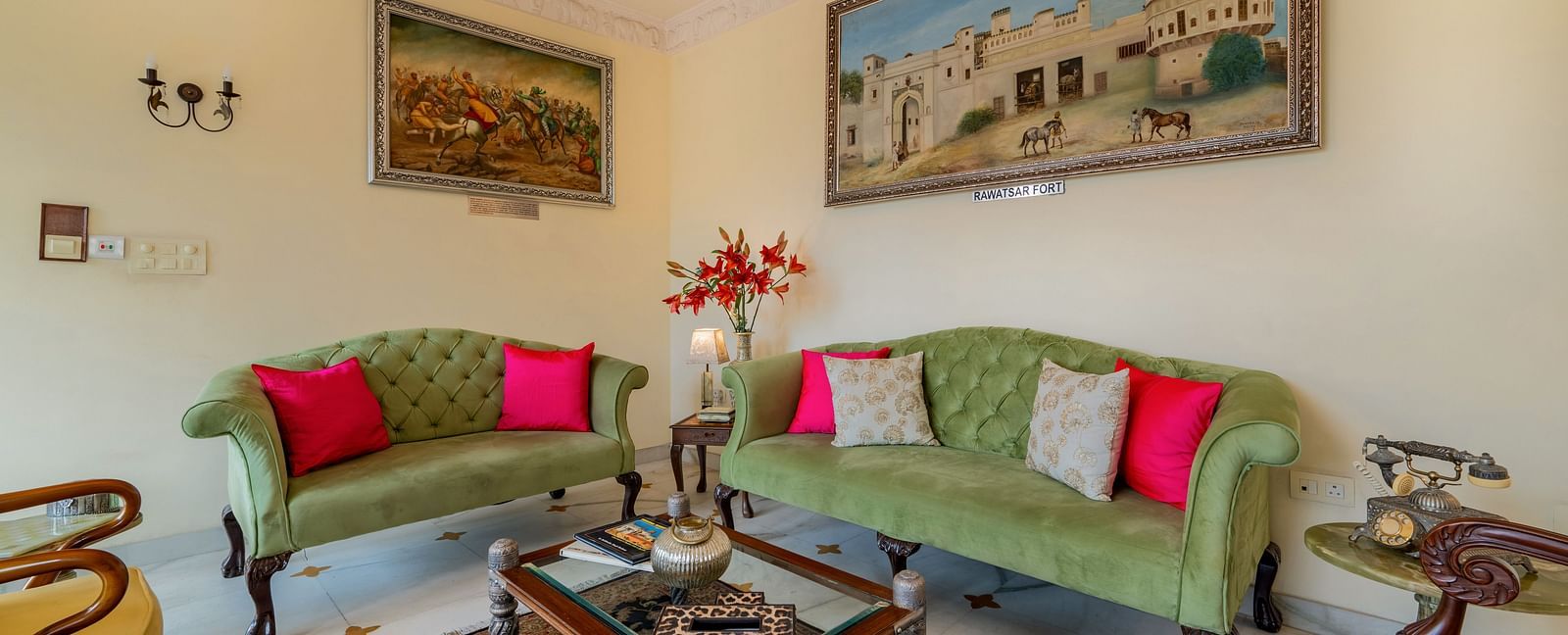 A living room with two green sofas, red cushions, framed artwork, and a glass-topped coffee table | Dera Rawatsar, Jaipur