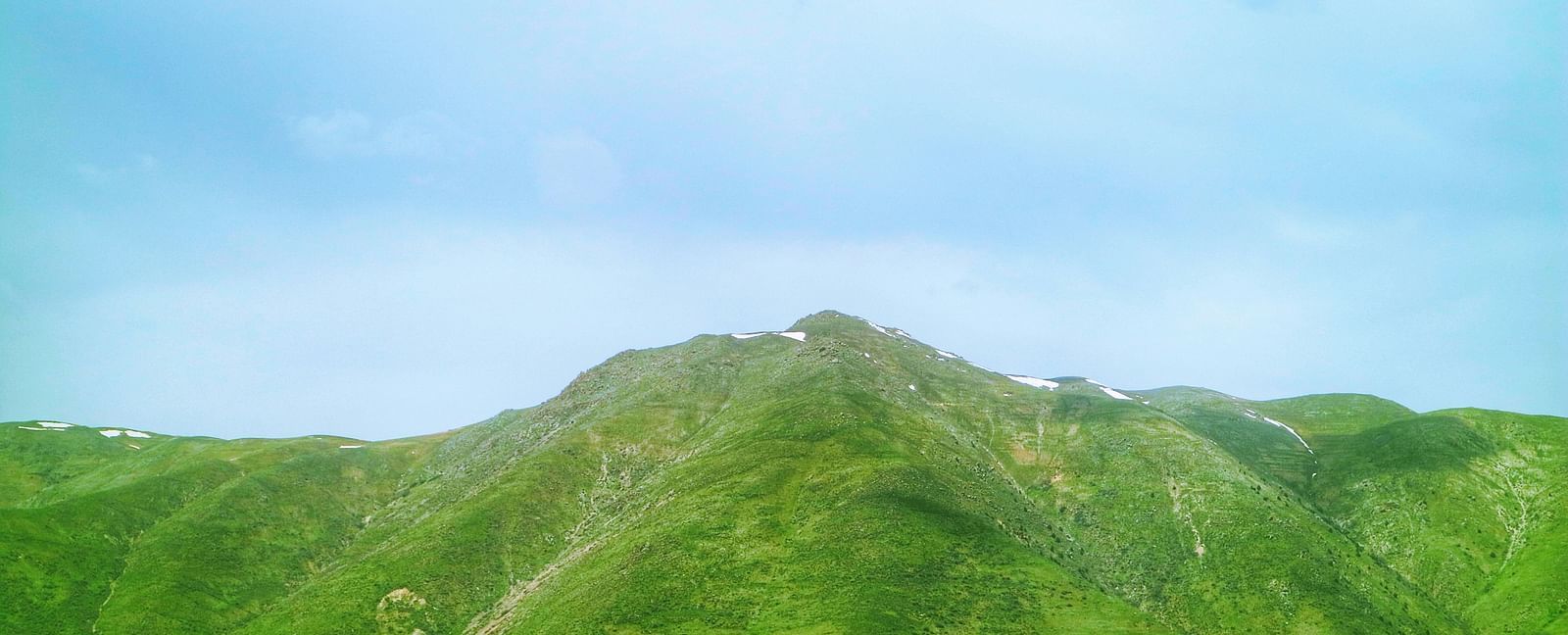 An overview of a rolling hill that is covered in greenery with blue sky in the background.