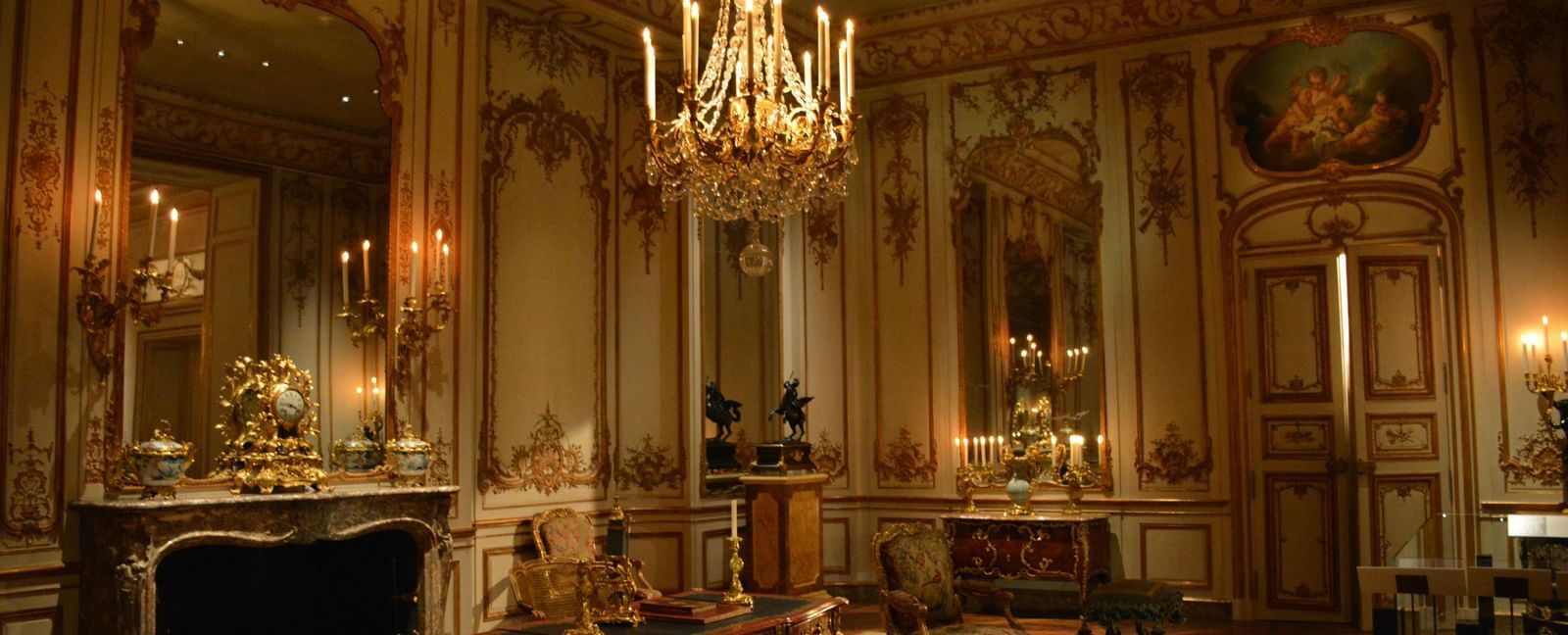 An elegant and lavishly decorated room with ornate furniture, a large fireplace, and a crystal chandelier, all highlighted by the rich, warm lighting.