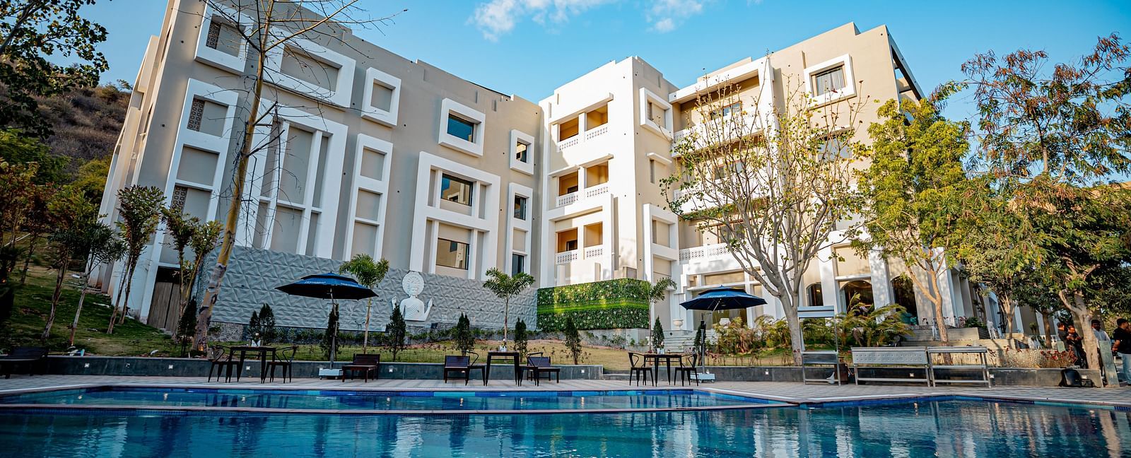 Facade view of Essentia Luxury Resort & Spa, Udaipur with a swimming pool in the front.