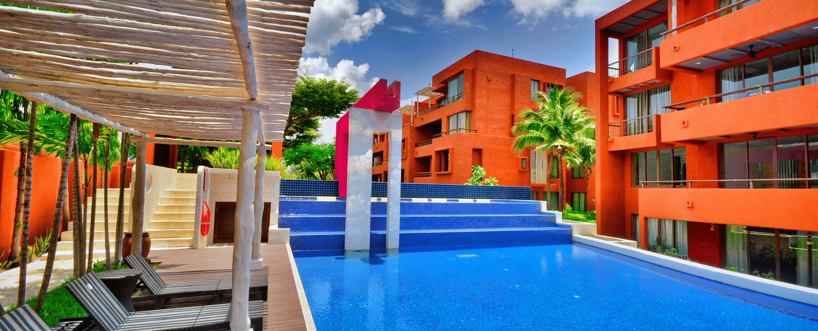 Vibrant hotel facade featuring sun loungers and a pool.