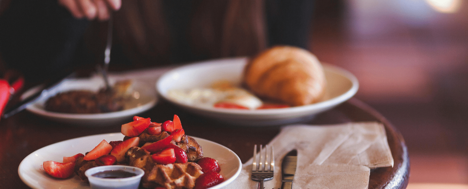 Waffle with strawberries and a croissant served on a round coffee table in a cafe. 