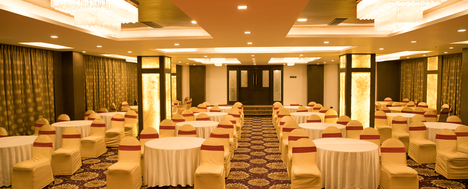 A banquet hall at Benzz Park Chennai set up with round tables and chairs with white covers, ready for an event.