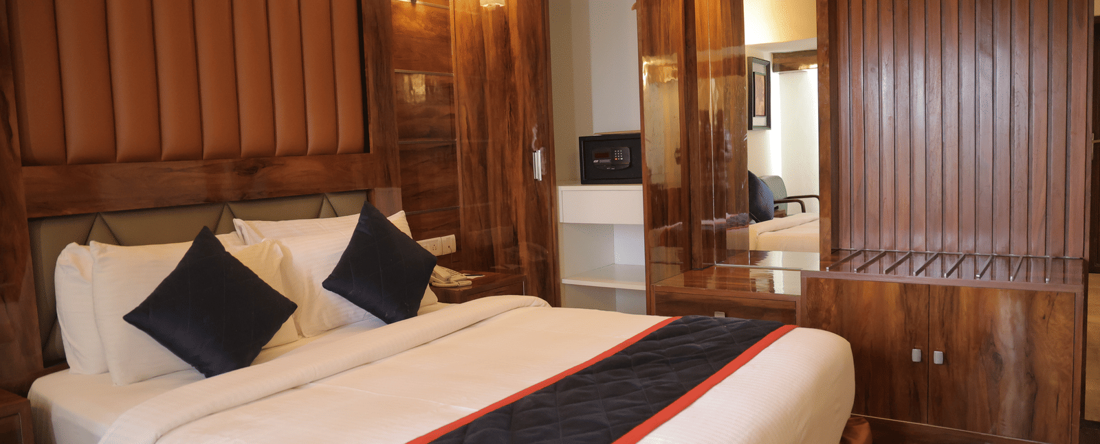 A spacious hotel suite with a large double bed, wooden panelling, and mirrored wardrobe doors - Benzz Park, Kodaikanal