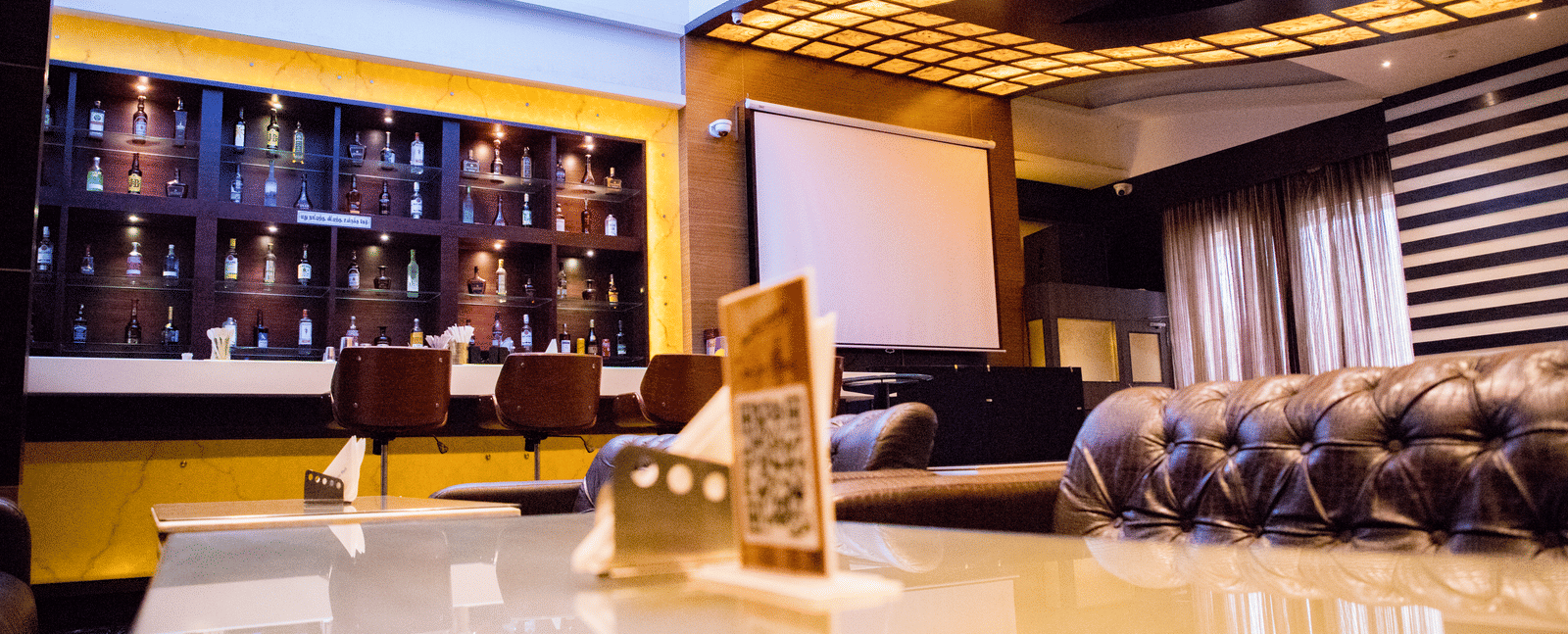 The bar at the Benzz Park, Vellore, taken from the dining table in the restaurant showcasing various liquor bottles on display behind the bar counter.