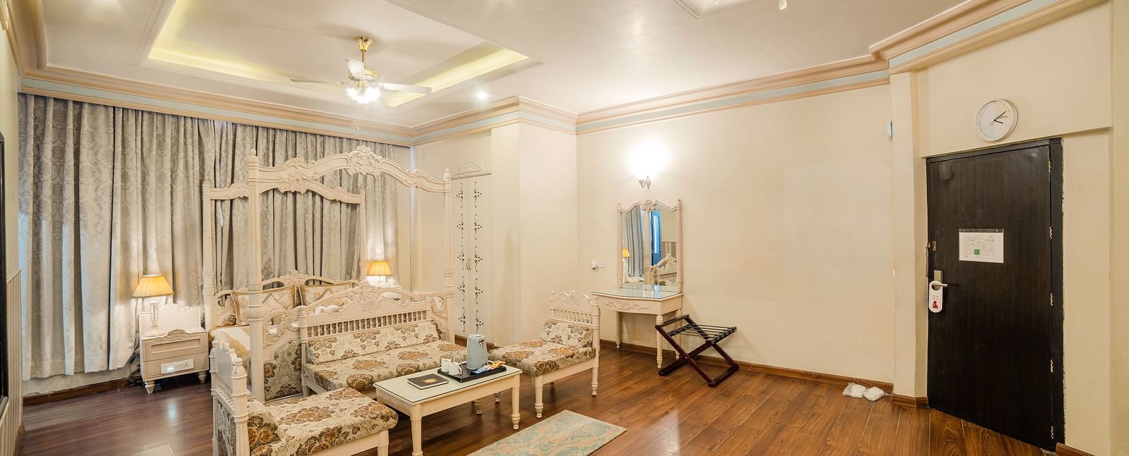 King Suite featuring a bed and a seating area with sofas and a coffee table, a wooden floor, and a door.- Hotel Ashok Nagpur