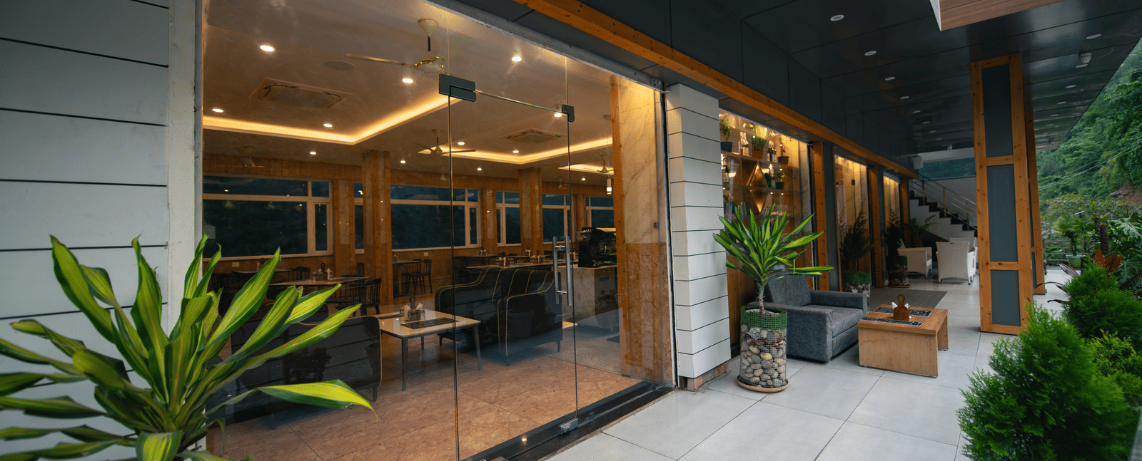 An entrance to the restaurant at The Tattva Devaprayag with big glass windows and some plants.