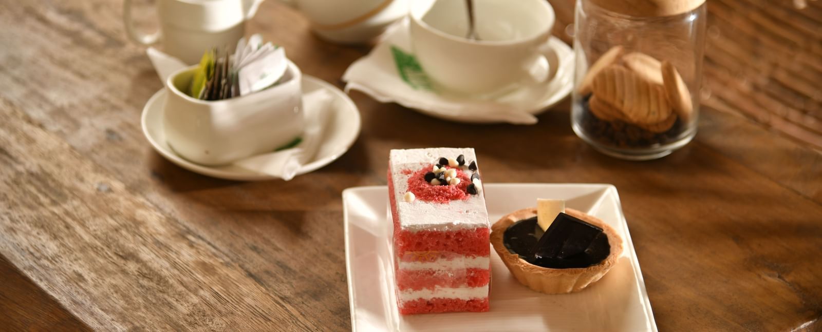 A tea set with cups, saucers, and a teapot is arranged on a table alongside a dessert | Chai
