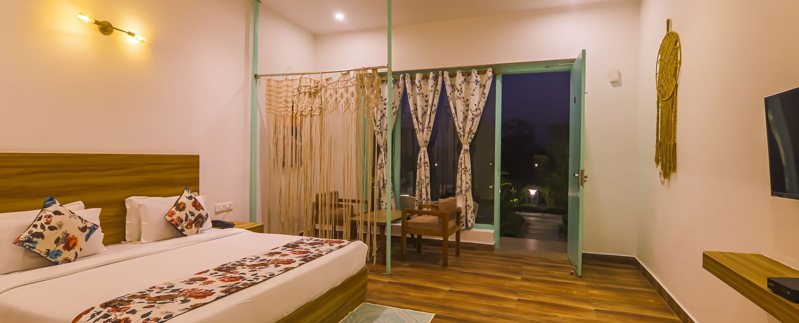 A well-lit bedroom at Vedikant Resorts The Mallard Corbett features a bed, seating area, and open balcony doors.