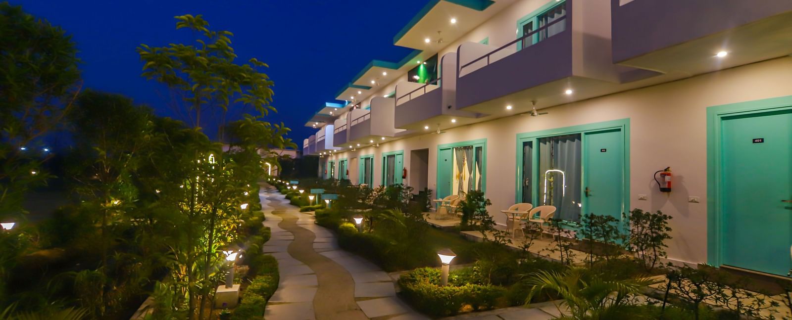 A walkway at Vedikant Resorts The Mallard Corbett at night is lined with rooms and subtle lighting.
