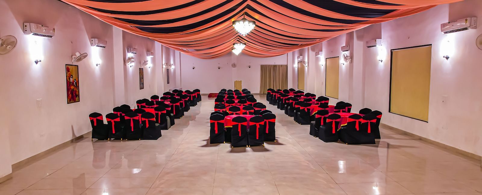 An empty banquet hall at Vedikant Resorts The Mallard Corbett has rows of chairs set up for an event under a decorated ceiling.