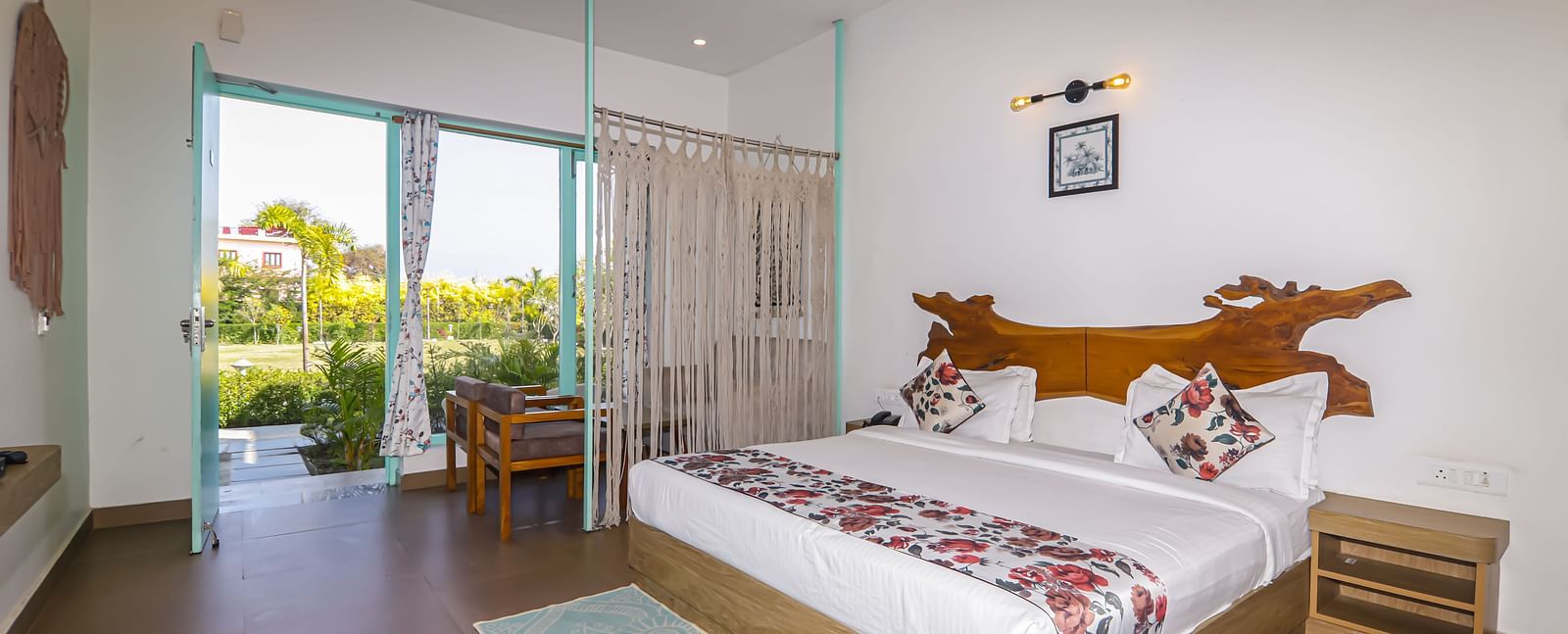 Brightly lit guest room at Vedikant Resorts The Mallard Corbett with a double bed, side table, and garden view through glass doors.