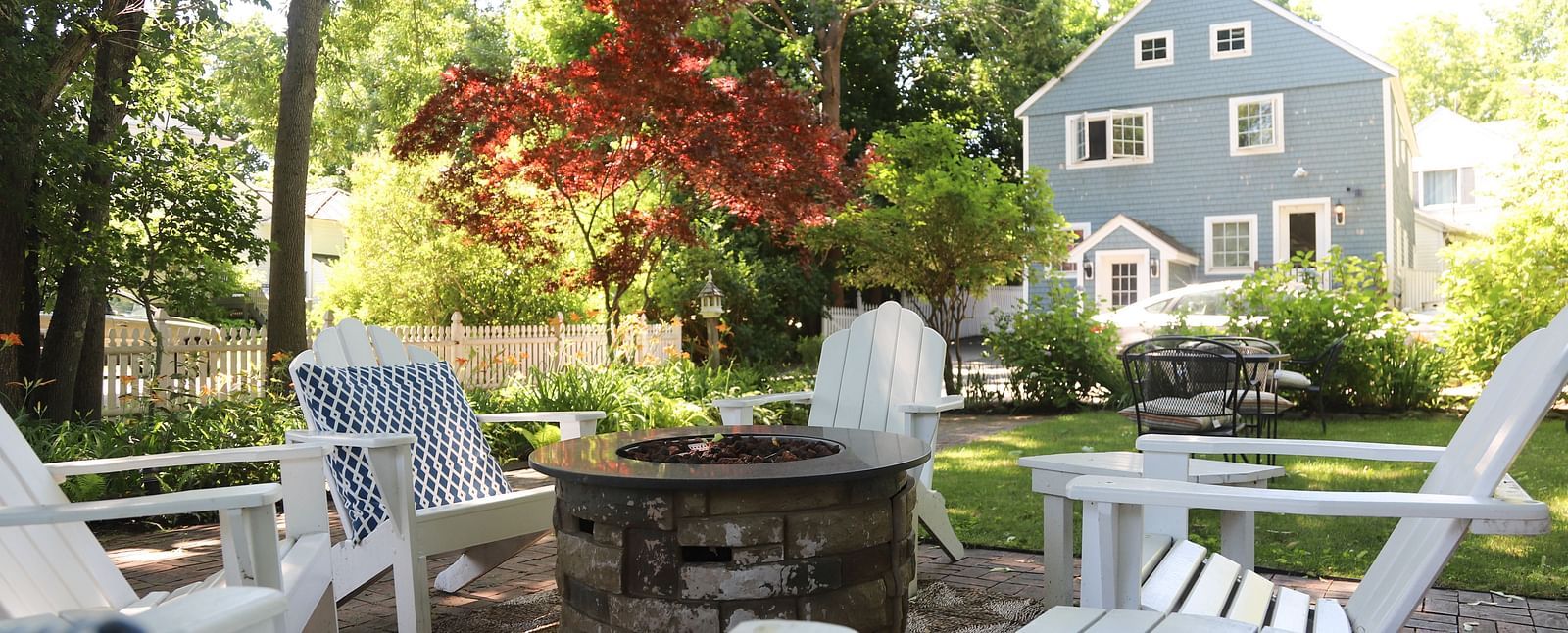 Outdoor garden seating area with white Adirondack chairs and a view of Hartstone Inn in the background.